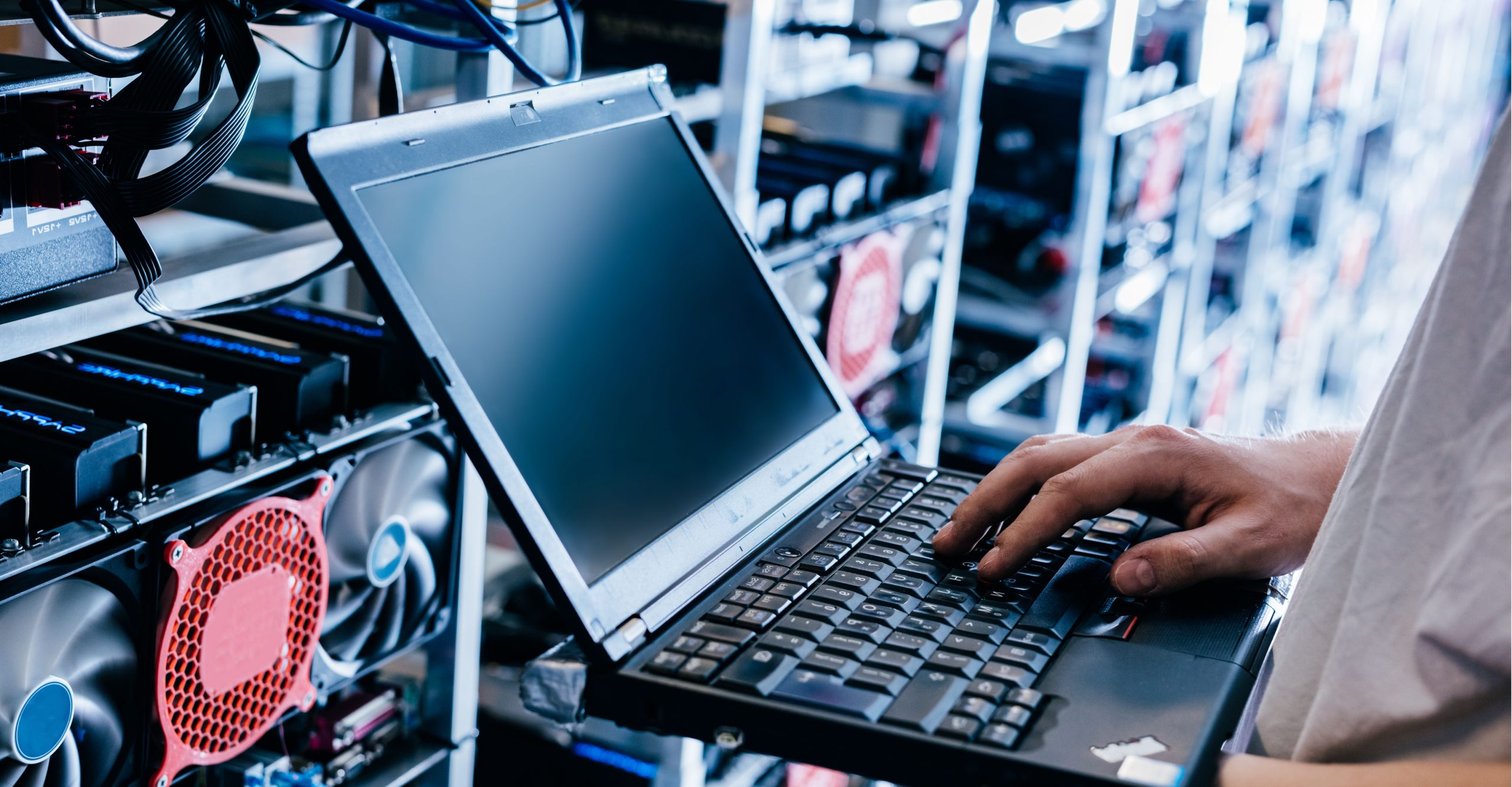 A person is using a laptop in a server room, surrounded by critical infrastructure and cooling fans, ensuring network uptime and availability.
