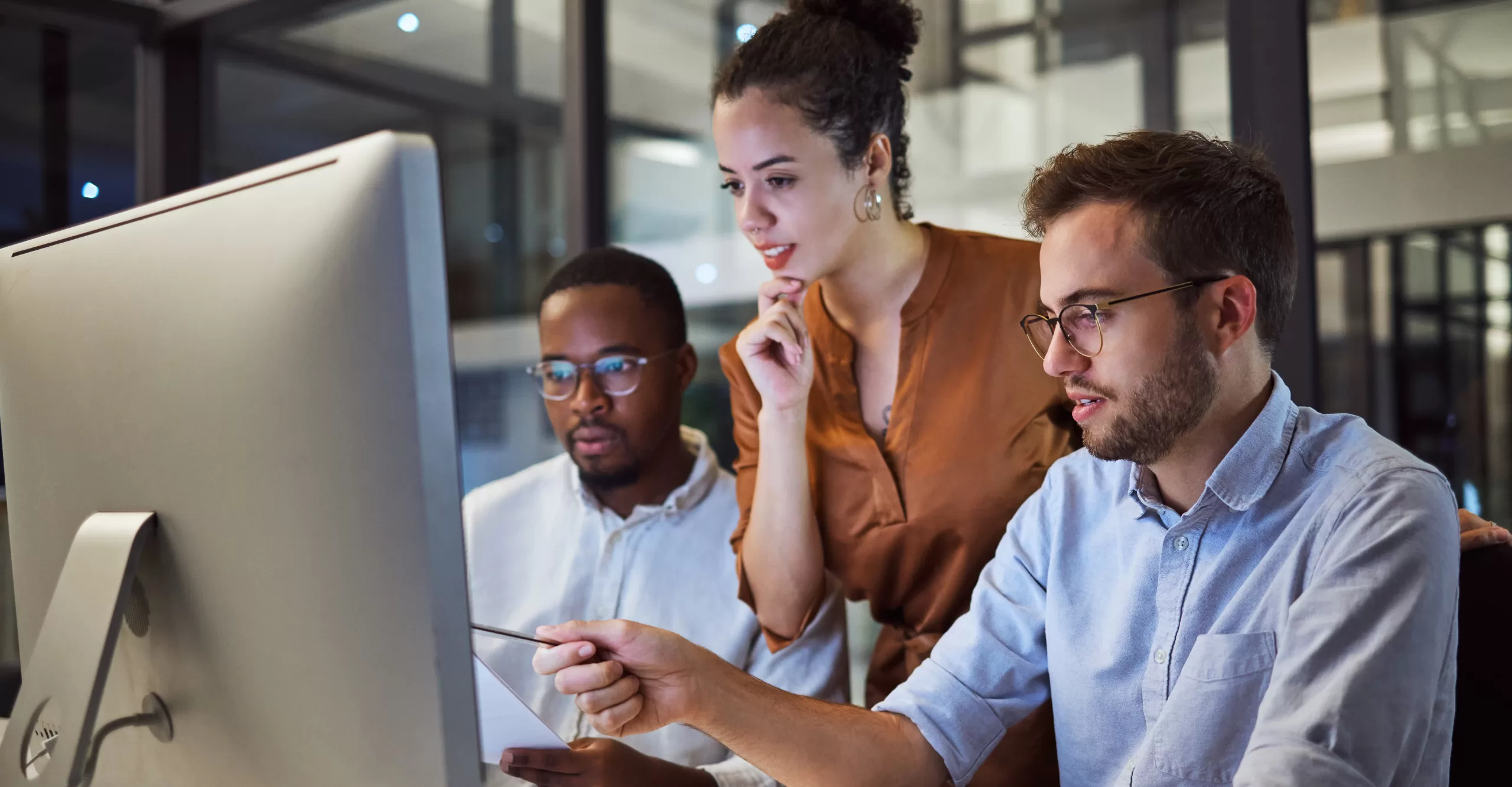 a group of young tech entrepreneurs group around a monitor to solve business problems together